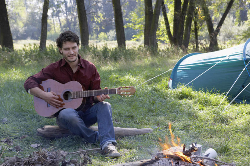 西方人,一个人,坐,抱,笑,微笑,露齿笑,横图,室外,白天,正面,旅游,度假,草地,草坪,树林,植物,欧洲,欧洲人,仅一个男性,仅一个人,阴影,光线,影子,帐篷,吉他,乐器,弦乐器,弹奏,演奏,注视,娱乐,草,树,树木,仅一个年轻男性,绿色,阳光,自然,观察,看,享受,休闲,放松,生长,成长,抱着,观看,察看,篝火,搂着,关注,弹拨弦鸣乐器,露营,野营,宿营,柴禾,男人,男性,年轻男性,白种人,搂,坐着,彩图,全身,柴火,弹拨弦乐器