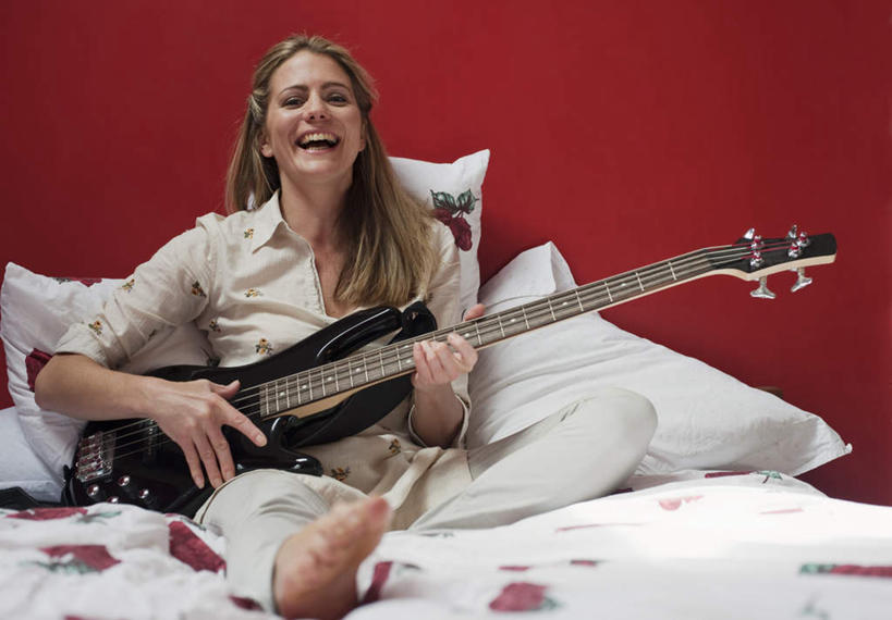 西方人,一个人,坐,笑,微笑,露齿笑,横图,室内,白天,正面,床,靠垫,卧室,欧洲,欧洲人,仅一个年轻女性,仅一个女性,仅一个人,一把,握,睡衣,服装,墙,双人床,床单,电吉他,靠枕,乐器,弦乐器,弹奏,拿,拿着,注视,被子,墙壁,墙面,衣服,红色,垫子,枕头,观察,看,握着,服饰,观看,察看,被单,衣着,穿着,关注,弹拨弦鸣乐器,寝衣,衣饰,年轻女性,女人,女性,白种人,坐着,彩图,全身,睡房,卧房,弹拨弦乐器