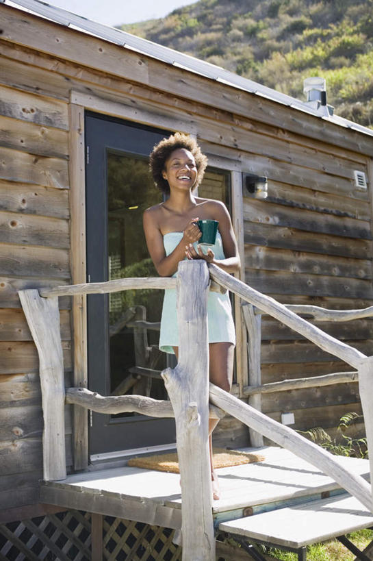 西方人,一个人,栏杆,站,笑,微笑,露齿笑,竖图,室外,白天,正面,旅游,度假,树林,地毯,门,建筑,杯子,玻璃,欧洲,非洲,黑人,欧洲人,仅一个人,服装,木制,浴巾,房屋,围栏,拿,拿着,注视,休闲装,娱乐,树,树木,衣服,马克杯,毛巾,观察,看,站着,享受,休闲,休闲服,陶瓷杯,放松,斜视,服饰,观看,支撑,察看,撑着,穿着,关注,裹着,年轻女性,女人,女性,非洲人,卷发,站立,彩图,全身,房子,木杆