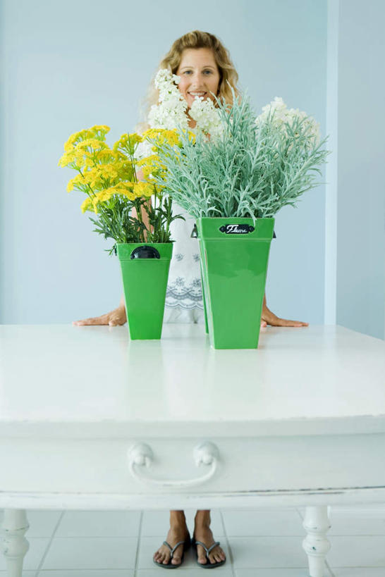 西方人,一个人,站,笑,微笑,露齿笑,竖图,室内,白天,正面,植物,桌面,桌子,叶子,欧洲,欧洲人,仅一个年轻女性,仅一个女性,仅一个人,盛开,绿叶,两束,花,花瓣,花朵,花卉,鲜花,黄色,白色,瓶子,塑料制品,花蕊,站着,嫩叶,塑料瓶,年轻女性,女人,女性,白种人,叶,叶片,站立,半身,彩图