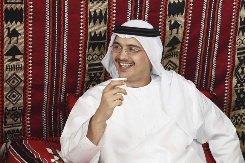 一个人,坐,笑,微笑,露齿笑,横图,室内,白天,正面,民族服装,壁纸,沙发,杯子,亚洲,仅一个男性,仅一个人,仅一个中年男性,握,头巾,墙,拿,拿着,注视,墙壁,墙面,纸制品,观察,看,握着,观看,纸杯,察看,关注,一次性杯子,布艺沙发,男人,男性,中年男性,阿拉伯人,白种人,亚洲人,墙纸,坐着,半身,彩图,传统服装,民俗服