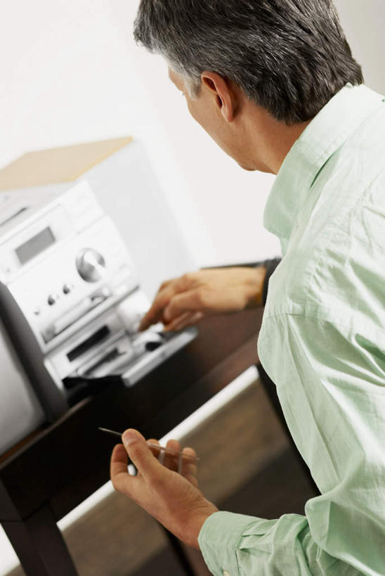 西方人,一个人,站,竖图,室内,白天,侧面,欧洲,欧洲人,仅一个男性,仅一个人,阴影,服装,朦胧,模糊,反射,影子,休闲装,衣服,站着,仅一个老年男性,休闲,休闲服,服饰,操作,影碟机,DVD播放器,DVD播放机,DVD影碟机,光盘存储器,数字多功能光盘,按键,老年男性,男人,男性,白种人,站立,半身,彩图