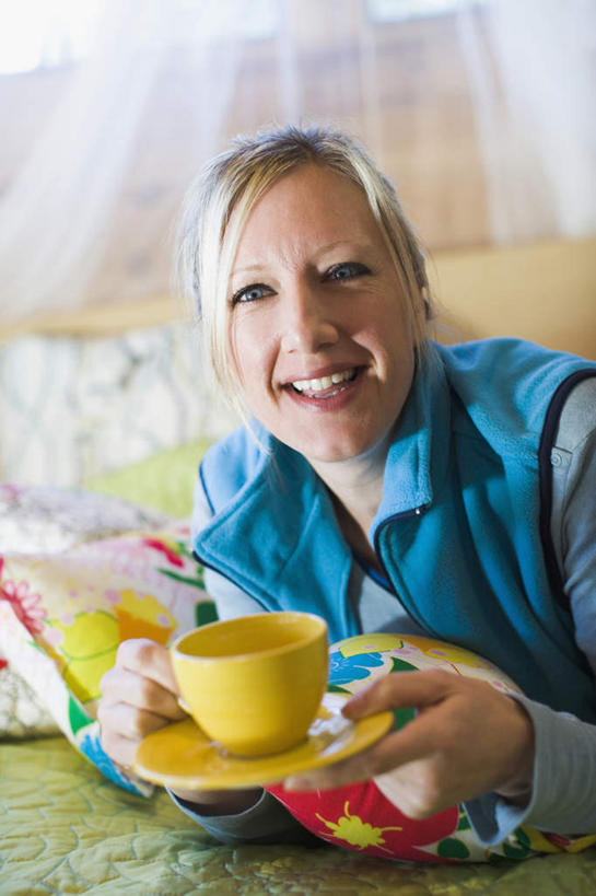 西方人,一个人,笑,微笑,露齿笑,竖图,室内,白天,正面,床,靠垫,卧室,杯子,餐具,纺织品,欧洲,欧洲人,仅一个女性,仅一个人,握,服装,朦胧,模糊,碟子,盘,蚊帐,双人床,床单,靠枕,织物,拿,拿着,注视,休闲装,被子,衣服,黄色,盘子,水杯,垫子,碟,枕头,观察,看,趴着,仅一个中年女性,休闲,休闲服,握着,服饰,观看,察看,被单,关注,阻隔,隔绝,女人,女性,中年女性,白种人,茶杯,趴,半身,彩图,睡房,卧房