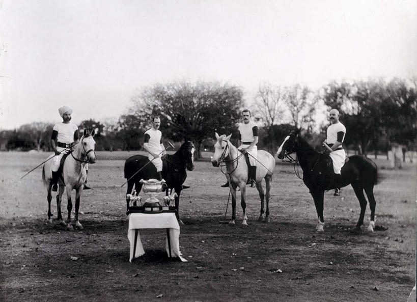 四个人,站,坐,横图,室外,白天,正面,运动服,成功,胜利,草地,草坪,植物,桌子,马,野生动物,亚洲,许多,阴影,服装,光线,木制,影子,很多,茶几,草,树,树木,四匹,一个,骑,衣服,蓝色,绿色,蓝天,天空,自然,动物,木制品,天,站着,光彩,运输,服饰,牲畜,生长,晴朗,单个,成长,衣着,穿着,泛黄,荣誉,奖品,老照片,万里无云,荣耀,衣饰,旧照,光荣,男人,男性,中年男性,阿拉伯人,白种人,亚洲人,晴空,晴空万里,站立,坐着,彩图,全身,奖杯,运动装