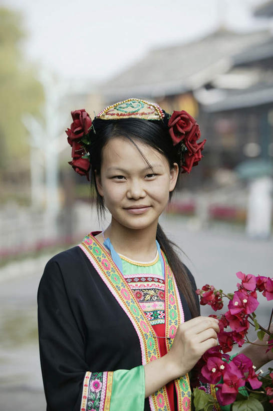 东方人,脸,头,脸颊,手,一个人,家,站,笑,微笑,露齿笑,竖图,室外,白天,正面,民族服装,植物,亚洲,仅一个年轻女性,仅一个女性,仅一个人,握,朦胧,模糊,装饰,盛开,房屋,屋子,拿,花蕾,拿着,注视,黄种人,楼房,少数民族,肩膀,住宅,花,花瓣,花朵,鲜花,树,树木,绿色,自然,花苞,花蕊,观察,看,站着,手部,握着,生长,成长,观看,华丽,修饰,点缀,察看,关注,衬托,美观,雅致,雅观,黎族,年轻女性,女人,女性,亚洲人,头部,脸部,脸蛋,面部,站立,半身,彩图,传统服装,民俗服,房子